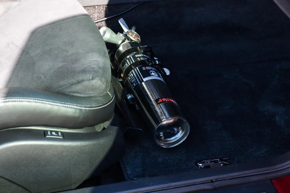 H3R Performance fire extinguisher mounted on the floor next to a black car seat, ready for track safety.