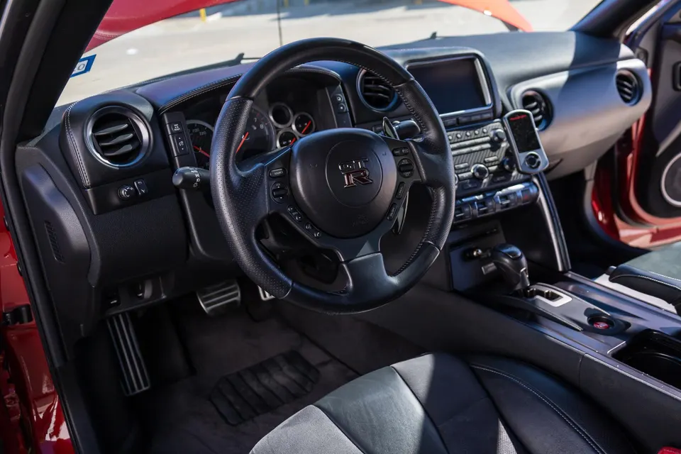 Nissan GT-R interior showing the steering wheel, dashboard, and a Cobb Accessport mounted on the center console.