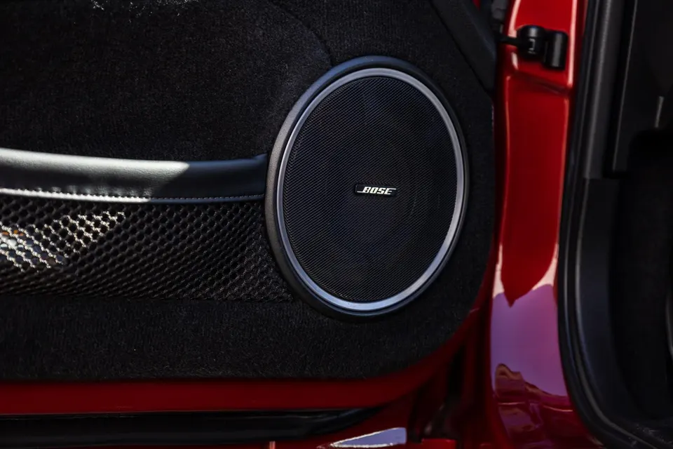 Close-up of a Bose speaker on the red car's interior door panel, showcasing the audio system.