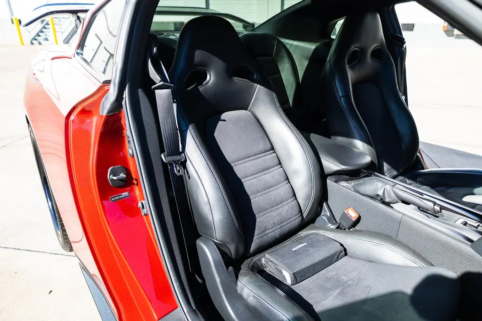 Interior view of a red Nissan GT-R with black leather and suede sport seats and door panel, showcasing the driver's side.