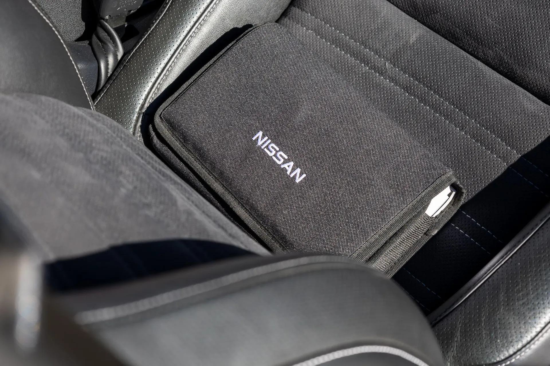 Nissan owner's manual case resting on a black leather car seat, showcasing interior detail.