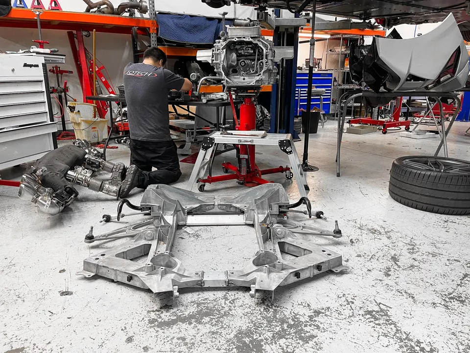 A mechanic works on a disassembled C8 Corvette in a performance tuning shop, with exhaust and subframe components on the floor.