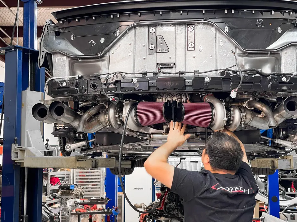 A mechanic installing a twin-turbo kit with large air filters and custom exhaust on a C8 Corvette on a lift at Jotech Motorsports.