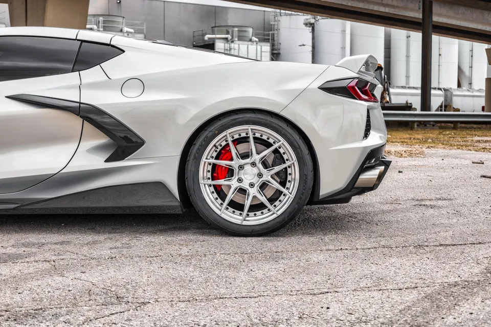 White C8 Corvette with aftermarket multi-spoke wheels, red brake calipers, carbon fiber side skirts, and a rear spoiler.