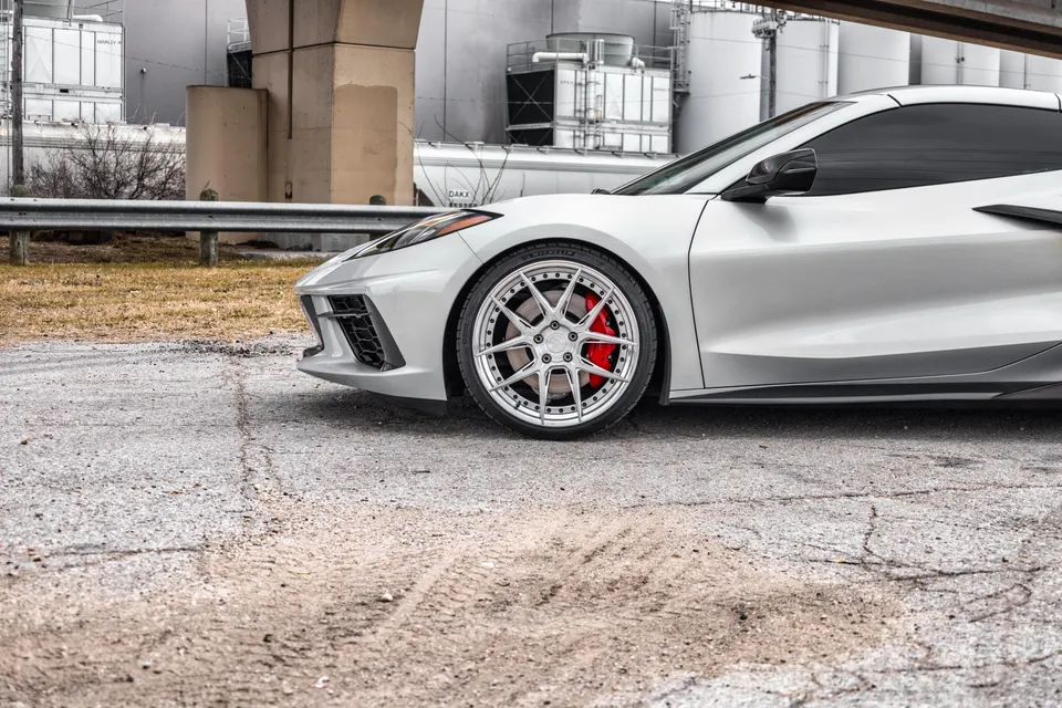 White Corvette C8 with custom multi-spoke wheels and red brake calipers parked in an industrial setting.