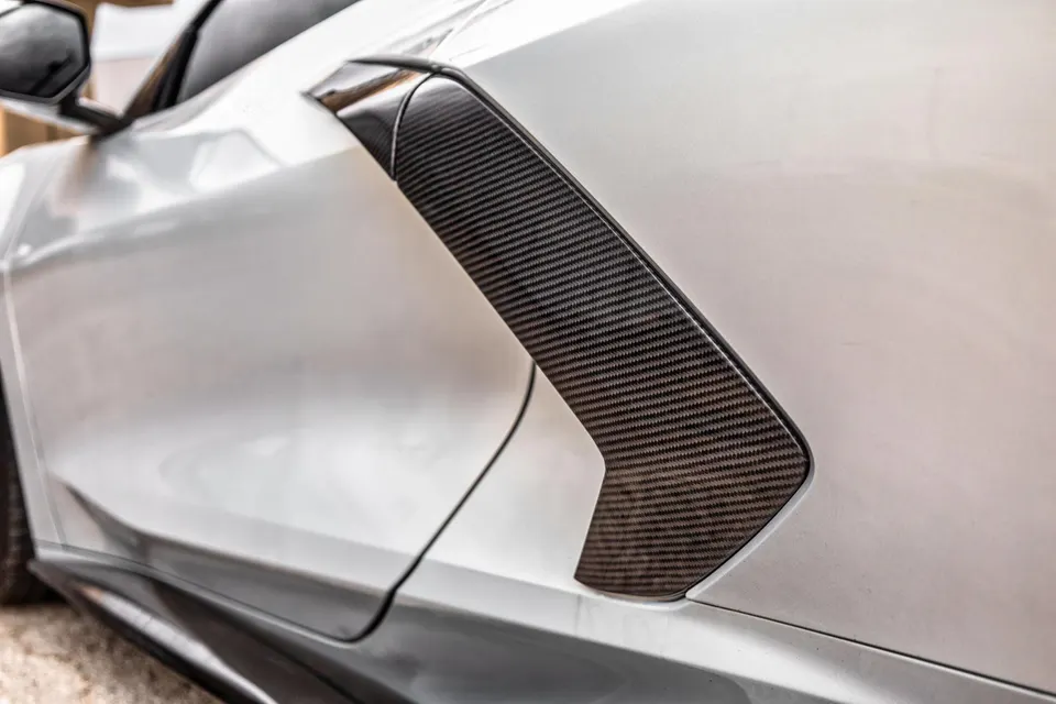 Close-up of a white car's side featuring a carbon fiber vent