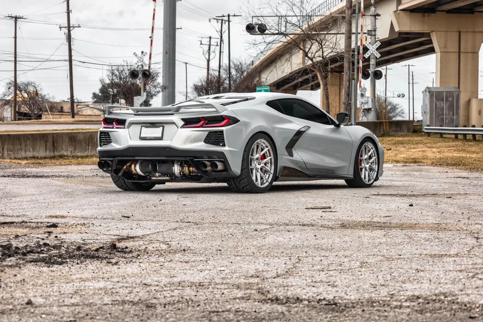 Silver Corvette C8.R with visible rear-mounted turbocharger and custom exhaust system, parked in an urban setting.