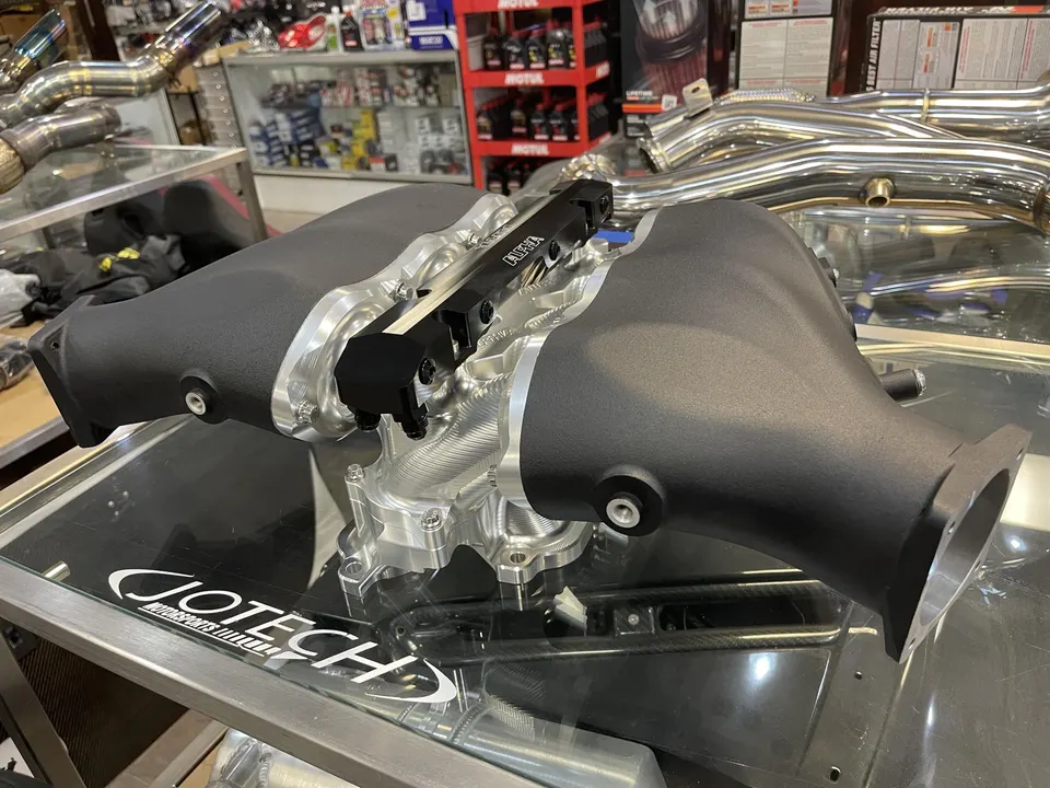 Aftermarket intake manifold with fuel rails displayed on a glass table at Jotech Motorsports performance shop.
