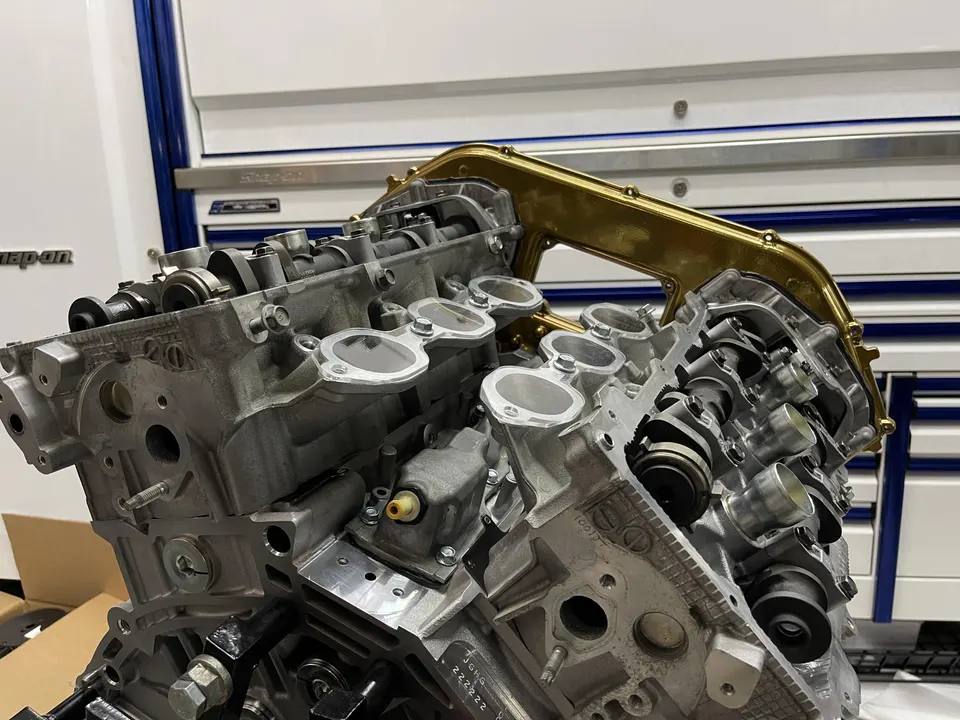 Close-up of a V8 engine assembly in a performance shop, showing cylinder heads, camshafts, and a gold intake manifold.