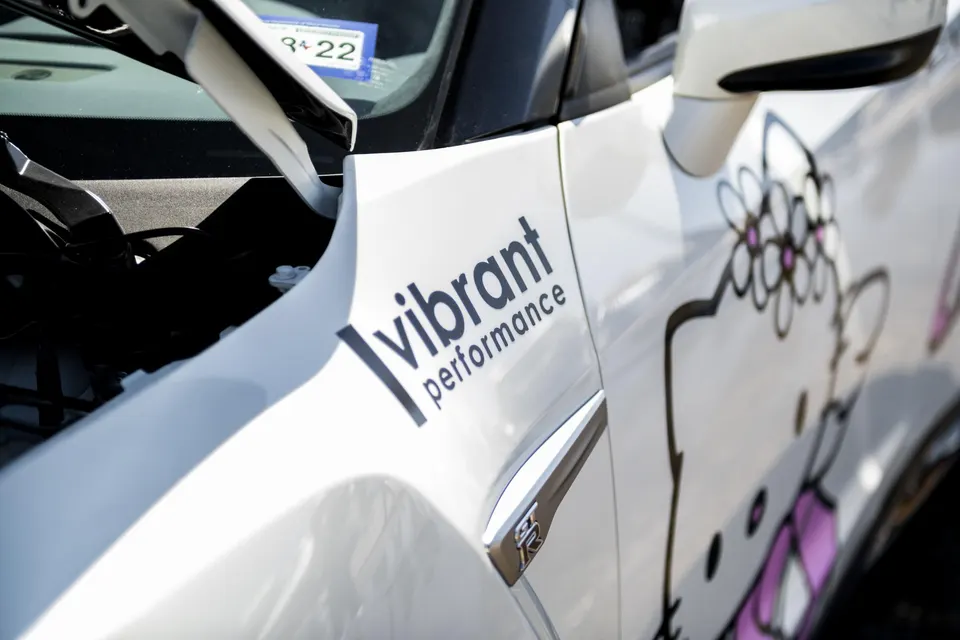 A white Nissan GT-R with a 'Vibrant Performance' decal and a Hello Kitty graphic on the side.
