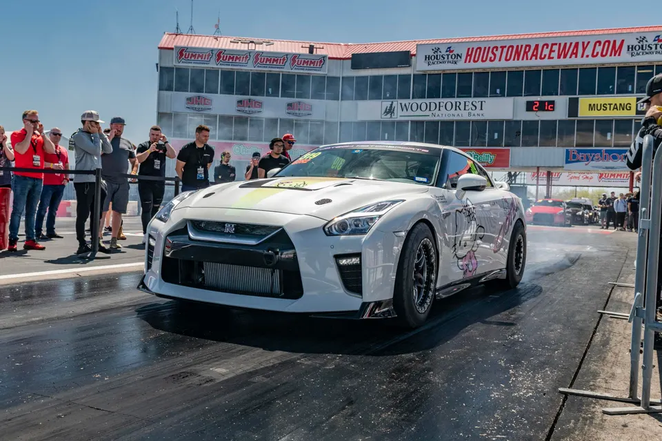 White Nissan GT-R performing a burnout at Houston Raceway Park, showcasing its large front-mounted intercooler.