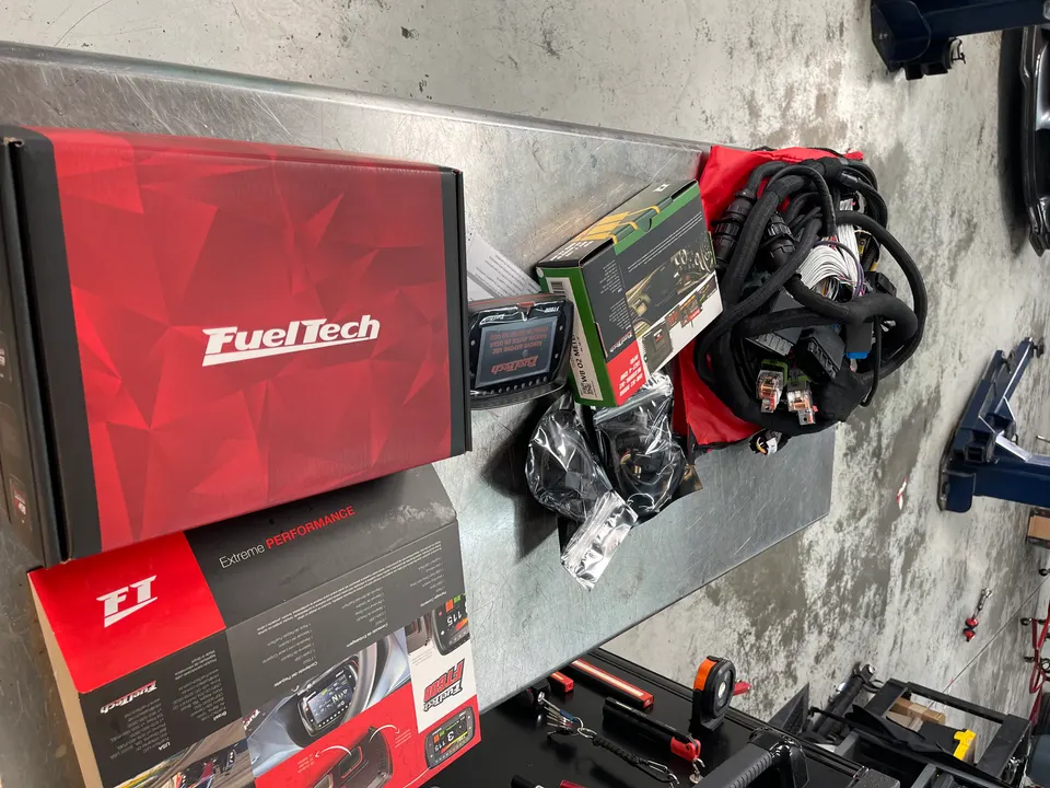 FuelTech ECU and wiring harness on a workbench in a performance tuning shop, ready for installation.