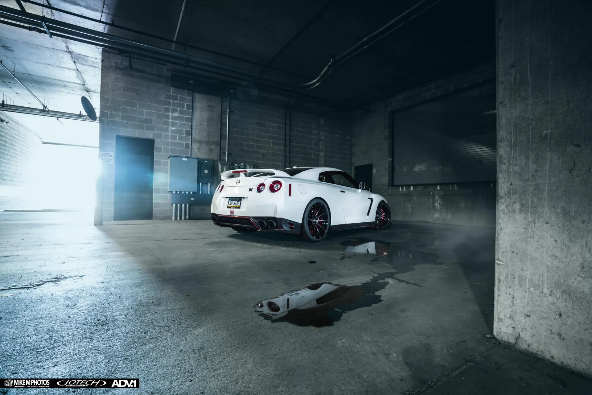 White Nissan GT-R with custom red wheels parked in a moody underground garage with reflections on the wet floor.