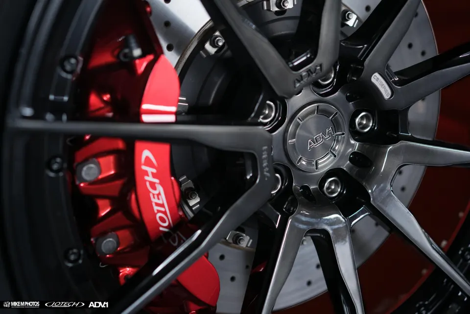 Close-up of a Jotech Motorsports car's ADV.1 wheels with red performance brake calipers and drilled rotors.
