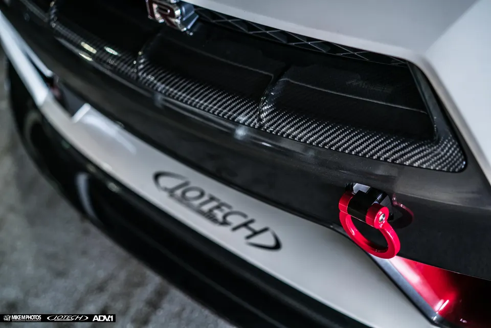 Close-up of a Nissan GT-R front bumper featuring carbon fiber trim, a red tow hook, and Jotech logo.