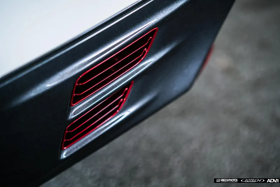 Close-up detail of a car's exterior vent with red accents on a dark grey body panel.