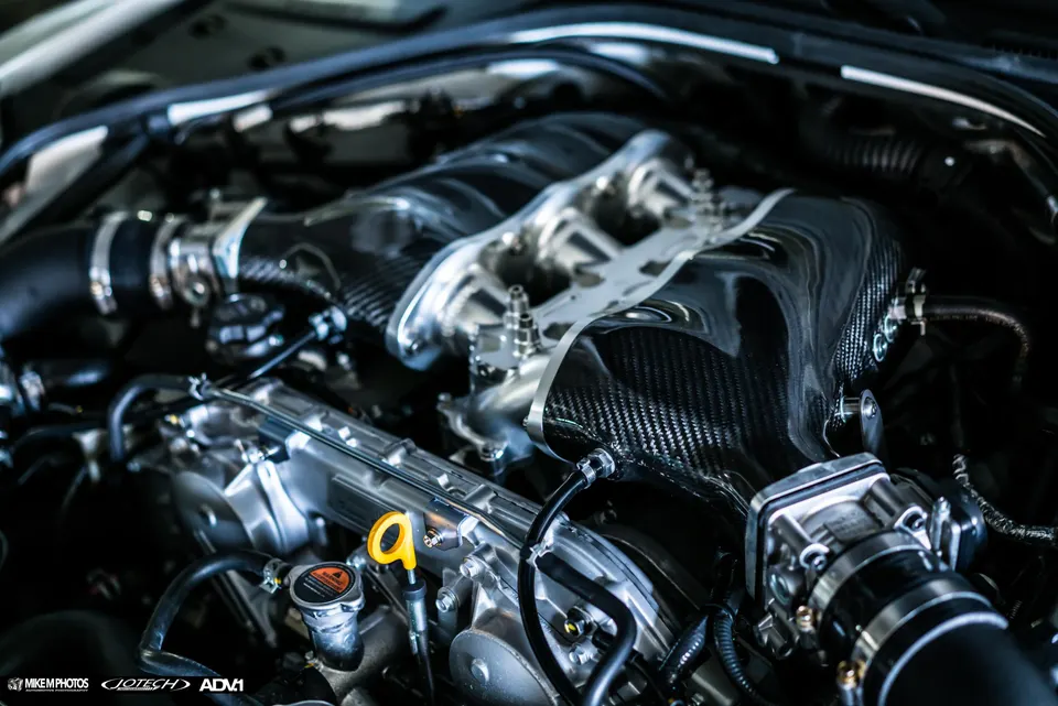 A close-up of a high-performance car engine bay featuring a carbon fiber intake manifold and custom induction system.