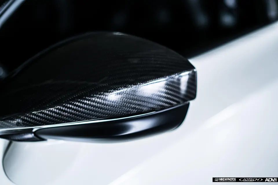 Close-up shot of a carbon fiber side mirror on a performance car, highlighting the weave pattern.
