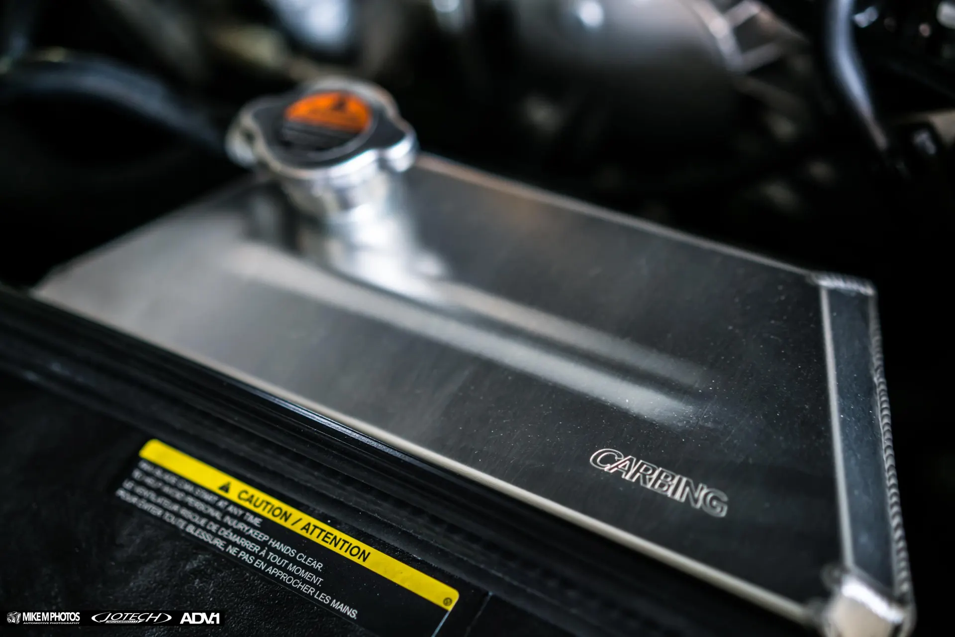 Close-up of a Carbing aluminum radiator and cap in a car's engine bay, highlighting the cooling system upgrade.