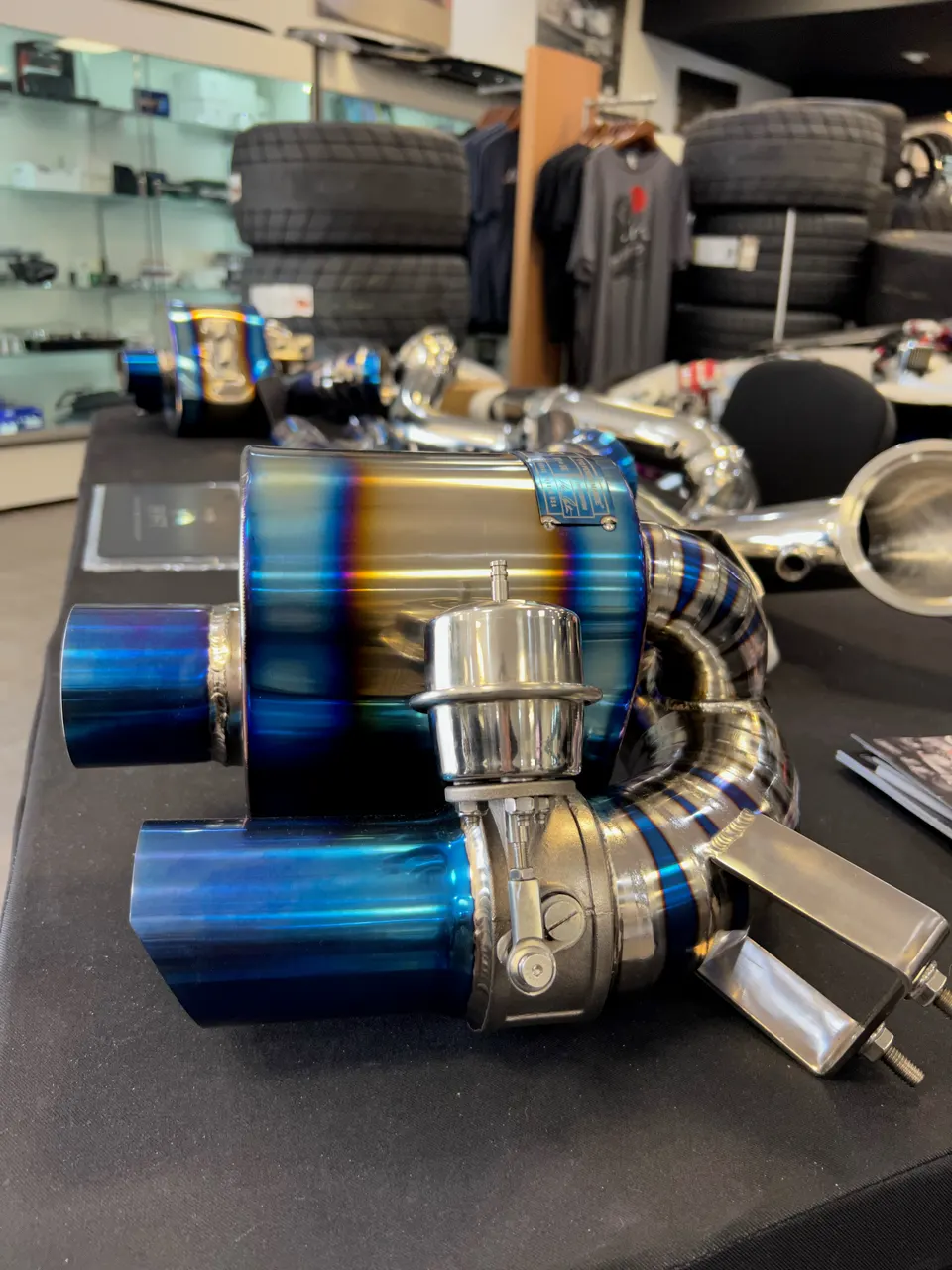 Close-up of a high-performance titanium exhaust system with burnt tips and a wastegate on display in a tuning shop.