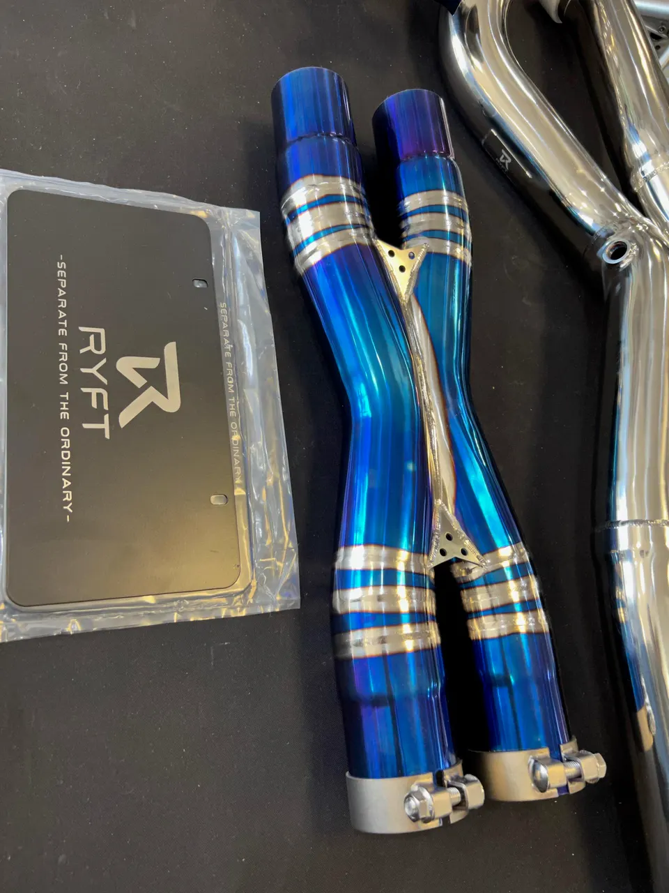 Ryft titanium exhaust X-pipe and components for a performance car build, showcasing the blue burnt finish.