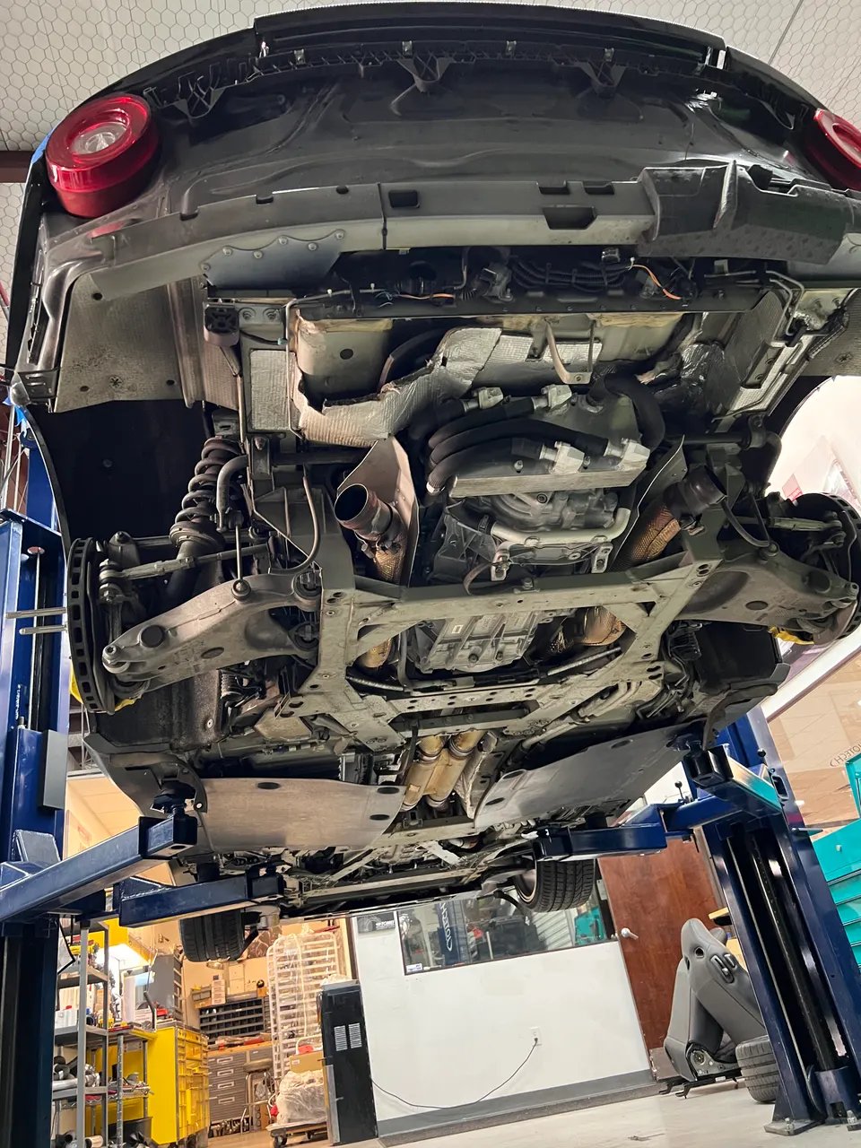 Underside view of a car on a lift in a shop, showcasing the exhaust system, suspension, and drivetrain components.