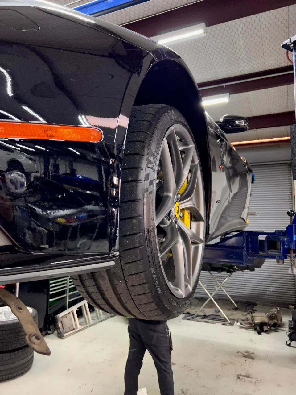 A black Ferrari on a lift in a performance tuning shop, showcasing its wheel, tire, and yellow brake caliper.