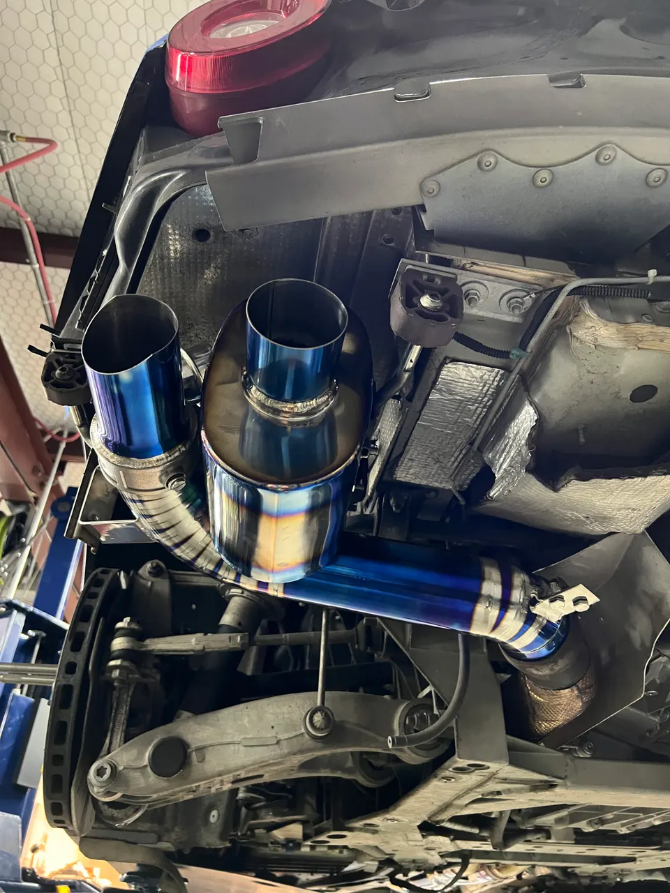 Aftermarket titanium exhaust system installed on a car's underbody in a performance shop