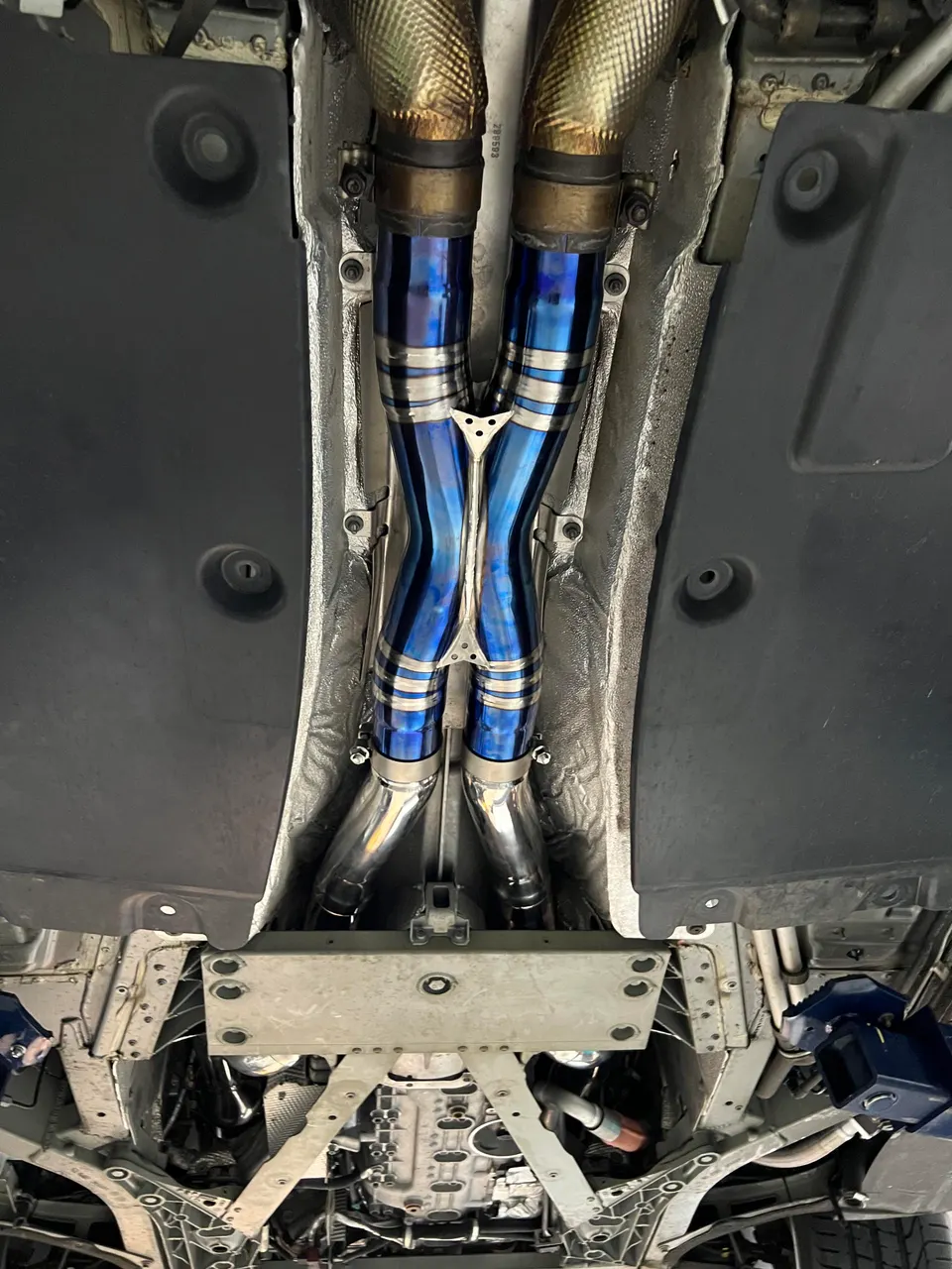 Underside view of a car on a lift showcasing a custom blue and silver titanium exhaust system.