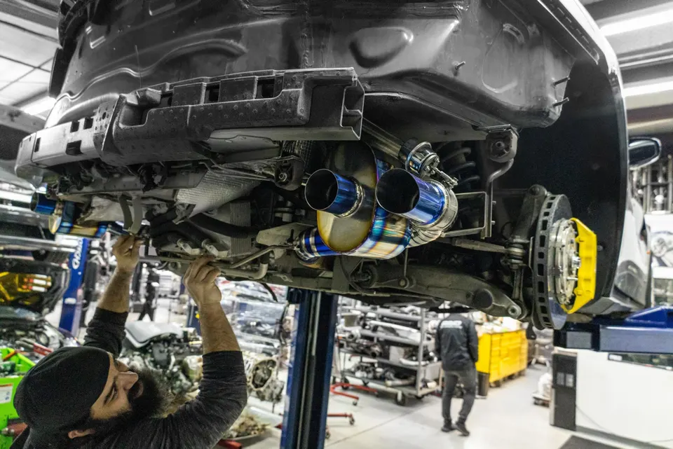 A mechanic installs a burnt titanium exhaust system on a car lifted in a performance tuning shop.