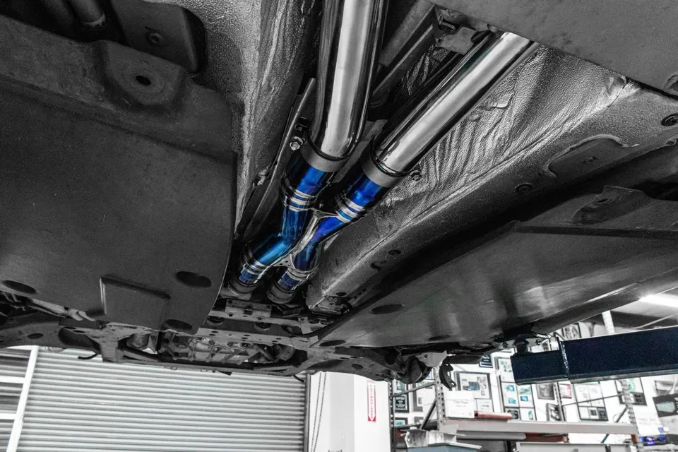 Underside view of a car on a lift, showcasing a custom blue performance exhaust system installed at a shop.