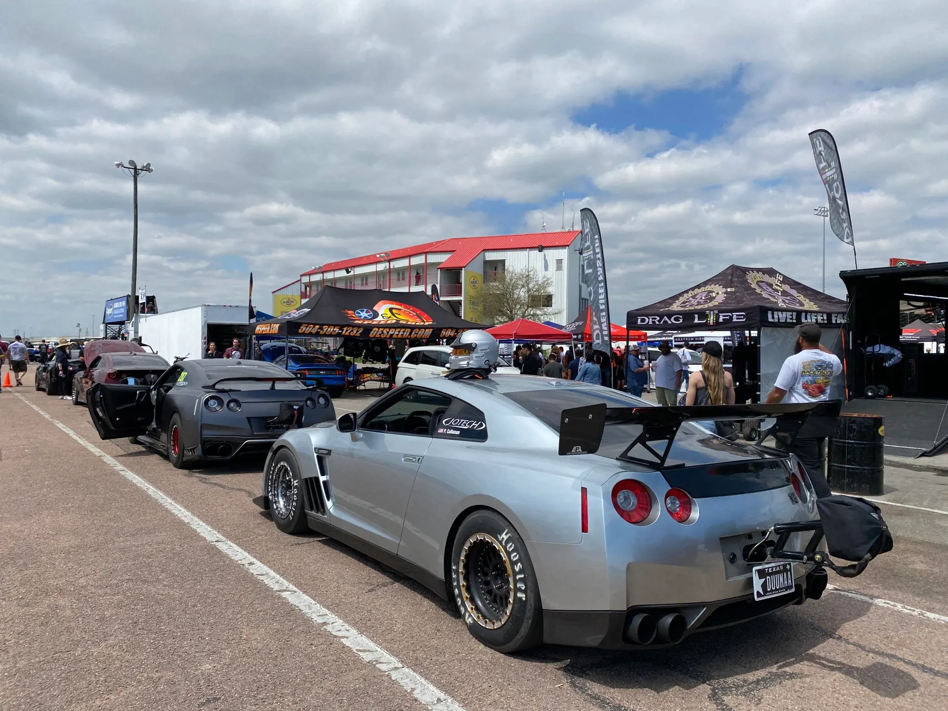 Modified Nissan GT-Rs lined up in the staging lane at a drag strip event with tents and spectators under a cloudy sky.