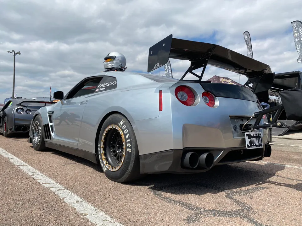 A silver Nissan GT-R drag car with a large rear wing and Hoosier drag slicks at a track event.