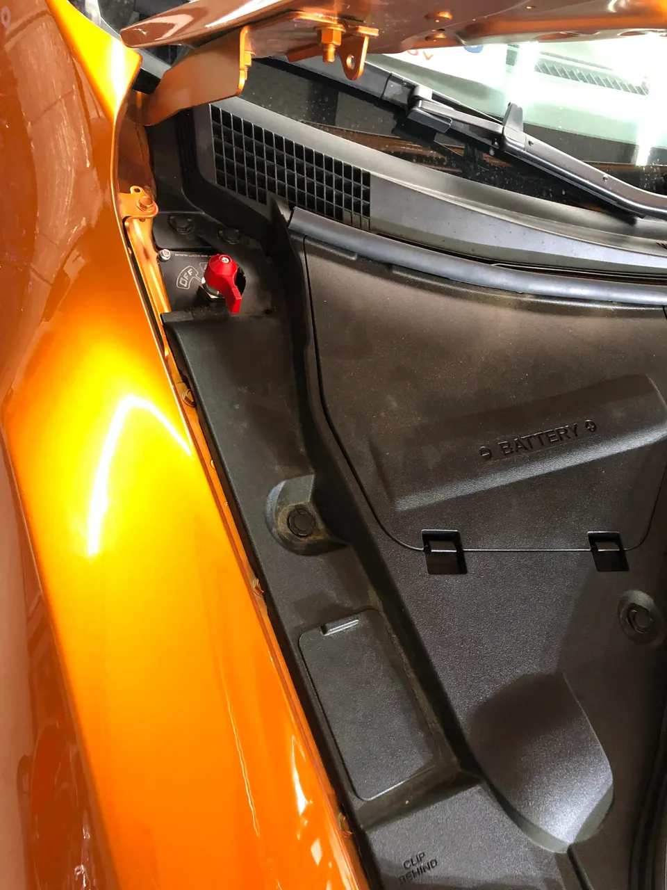 Close-up of a red battery kill switch installed in the engine bay of an orange performance car.