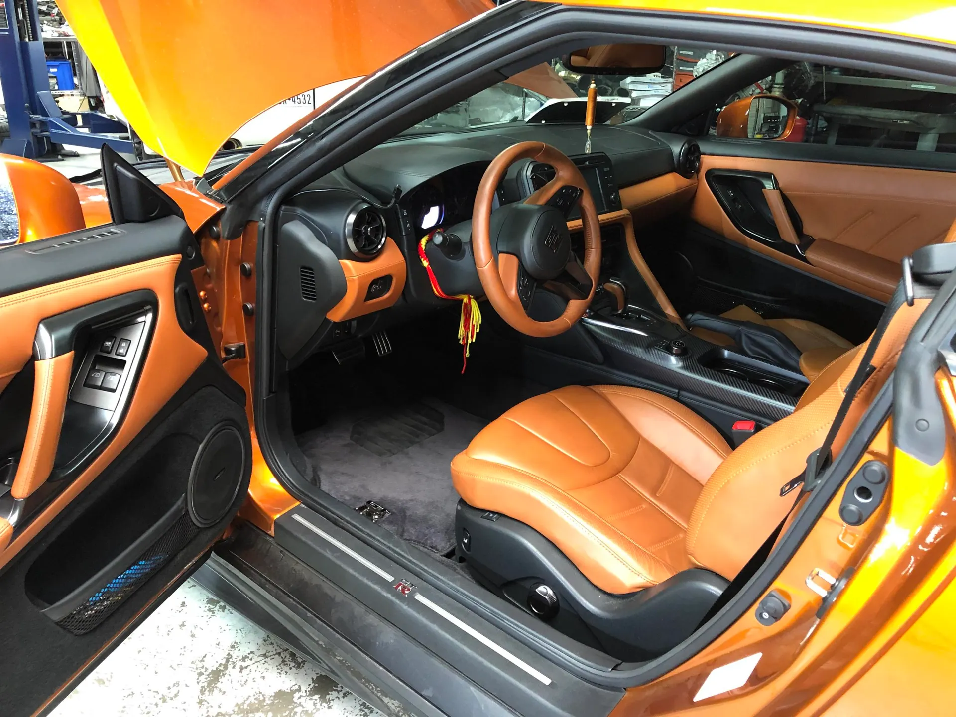 Nissan GT-R interior with orange and tan leather, steering wheel, and door panel in a shop setting.