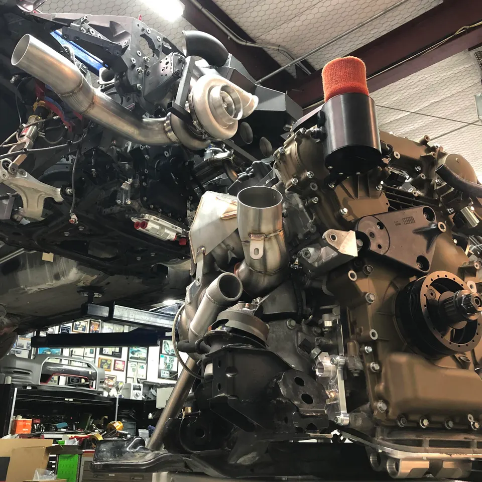 A detailed view of a high-performance engine with a large turbocharger and custom exhaust piping being assembled in a shop.