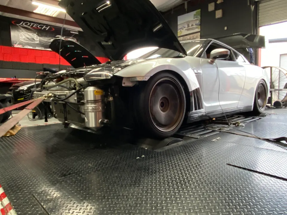 A silver Nissan GT-R with its hood open, strapped to a dyno for performance testing at Jotech Motorsports.