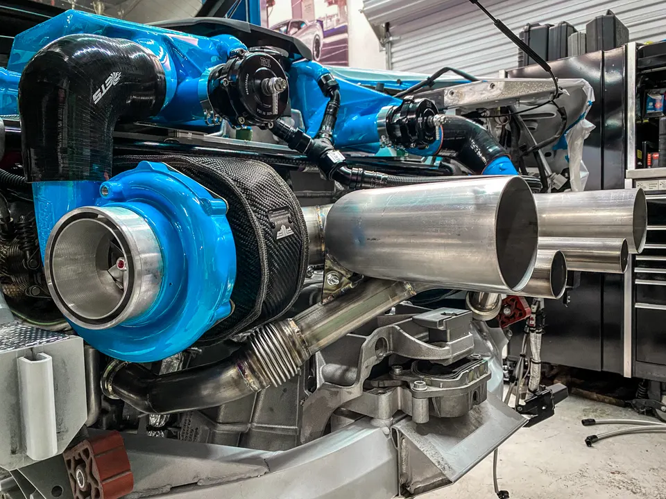Close-up of a custom blue turbocharger and stainless steel exhaust system on a high-performance engine in a shop.