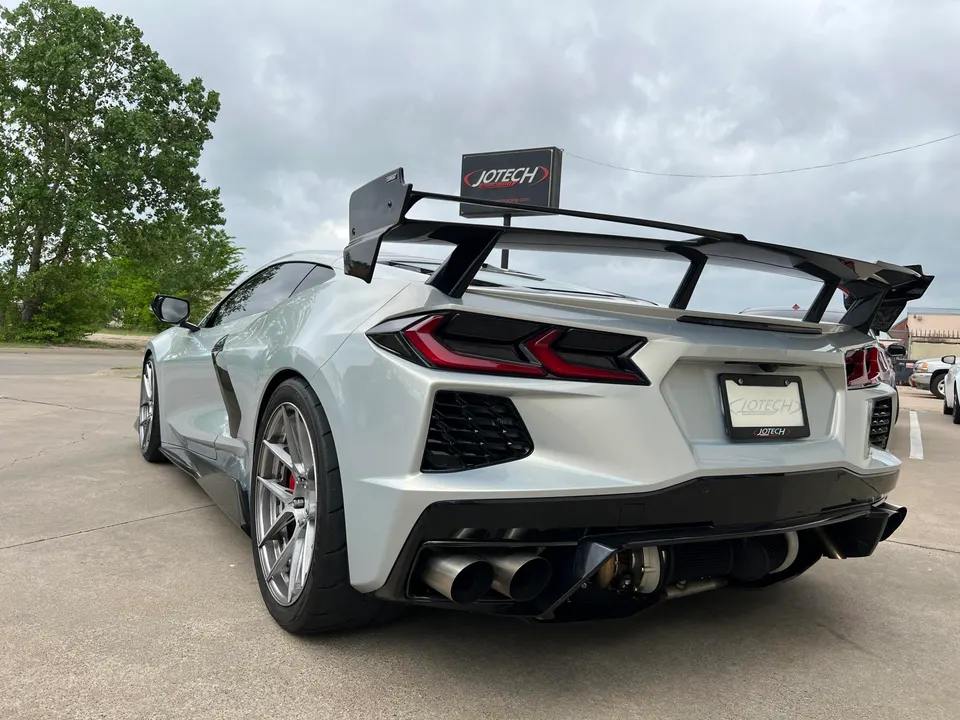 A silver Corvette C8 with a large rear wing, aftermarket wheels, and visible turbo exhaust system parked outside Jotech Motorsports.