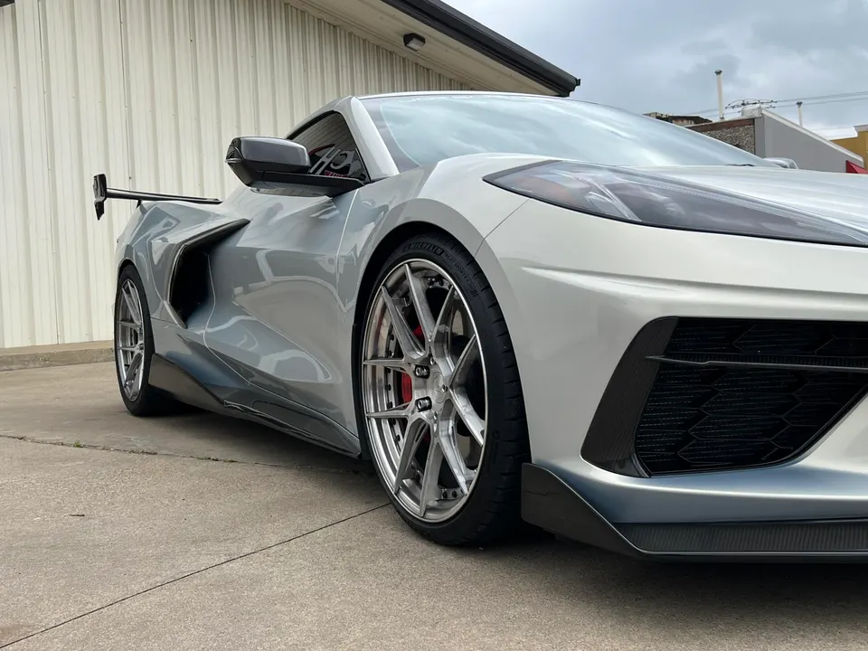Silver Chevrolet Corvette C8 with aftermarket wheels, carbon fiber front splitter, side skirts, and rear wing.
