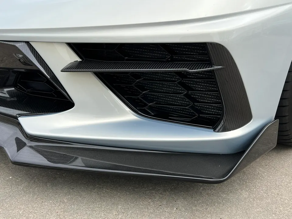 Close-up of a car's front bumper with carbon fiber splitter and grille trim