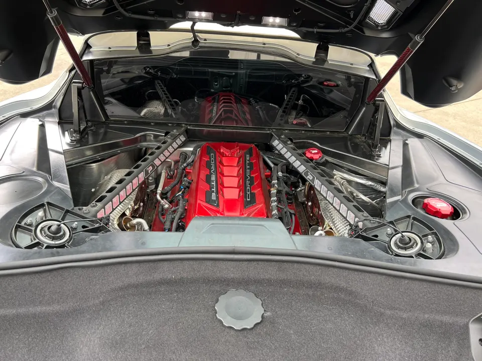 Detailed view of a red engine in a Corvette C8 mid-engine bay with the rear hatch open, showcasing the engine assembly.