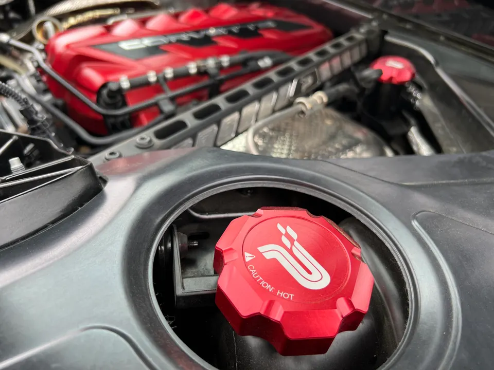Close-up of a red aftermarket coolant cap and engine cover in a Corvette C8 engine bay.