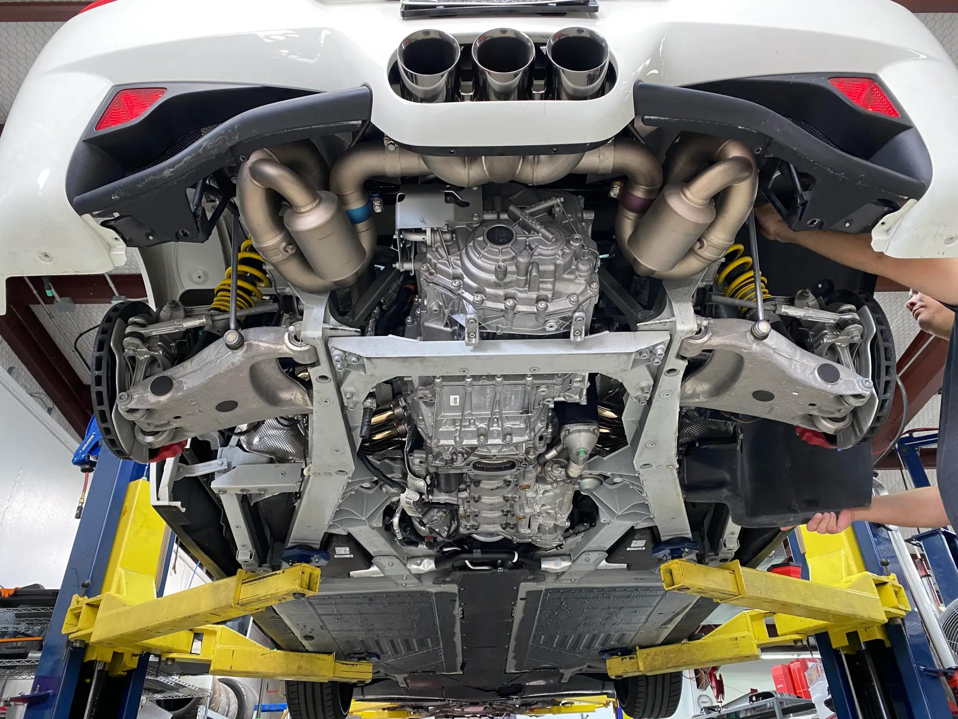 Underside view of a Porsche 911 on a lift in a shop, showcasing the aftermarket exhaust system and suspension.