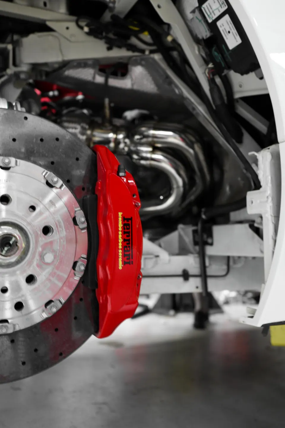 Close-up of a red Ferrari Brembo carbon ceramic brake caliper and perforated rotor with stainless steel exhaust headers.
