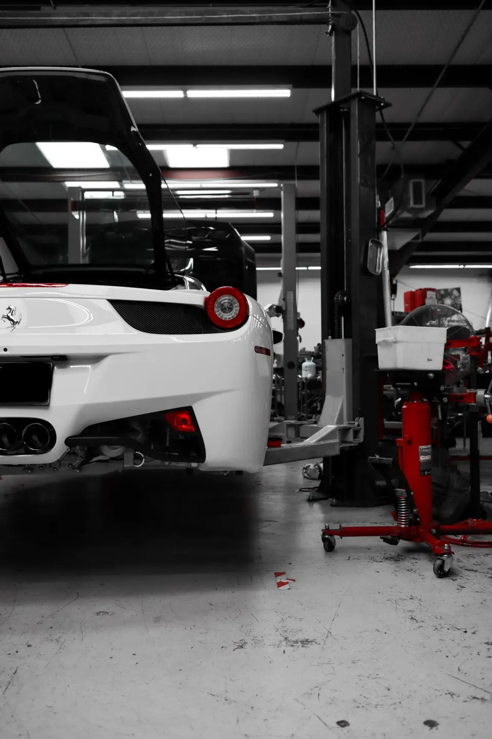 A white Ferrari 458 Italia with its engine bay open, on a lift in a performance tuning shop.