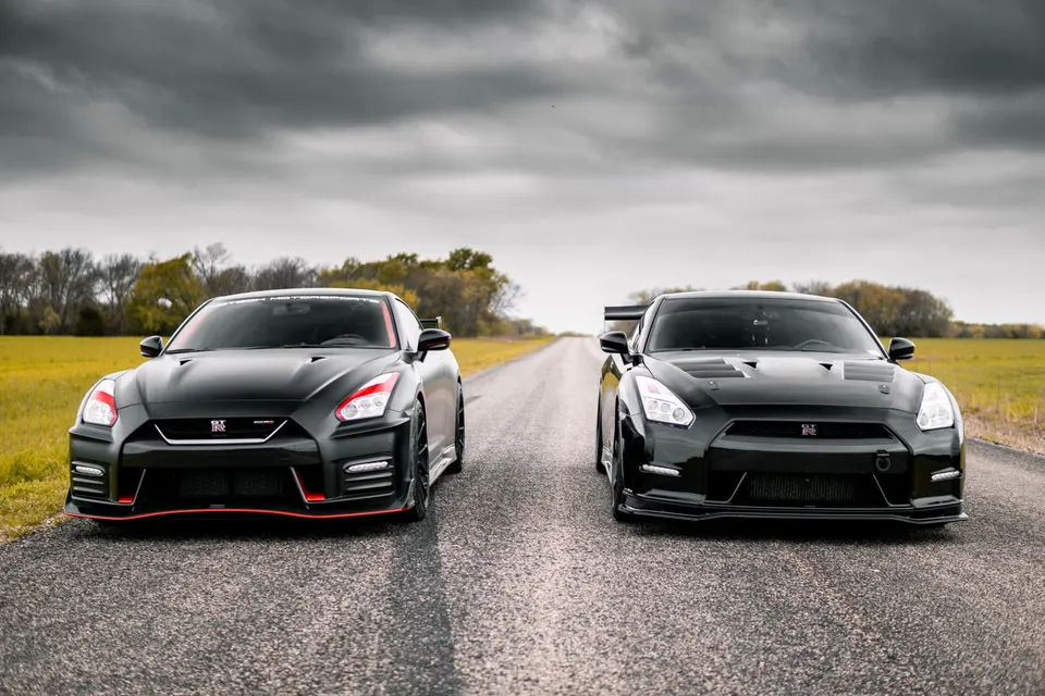 Two black modified Nissan GT-R R35s parked side-by-side on a rural road under a cloudy sky.