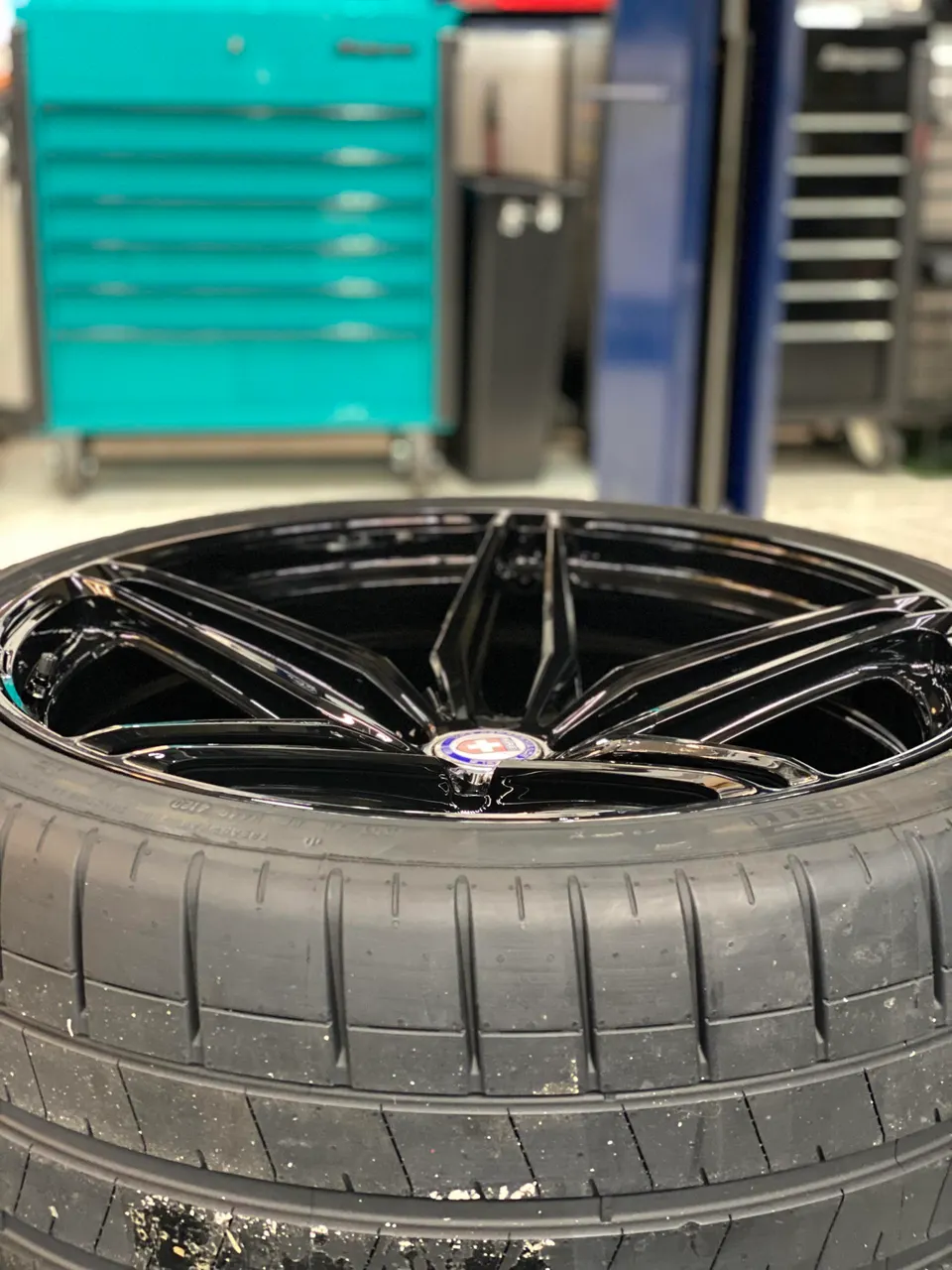 Close-up of a black HRE performance wheel mounted with a Pirelli tire in a shop setting.