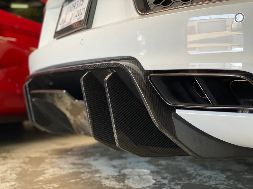 Close-up of a white performance car's rear bumper featuring a carbon fiber diffuser and dual exhaust tips.