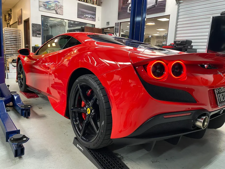 Red Ferrari F8 Tributo on a lift in a performance tuning shop, showcasing its rear design and wheels.